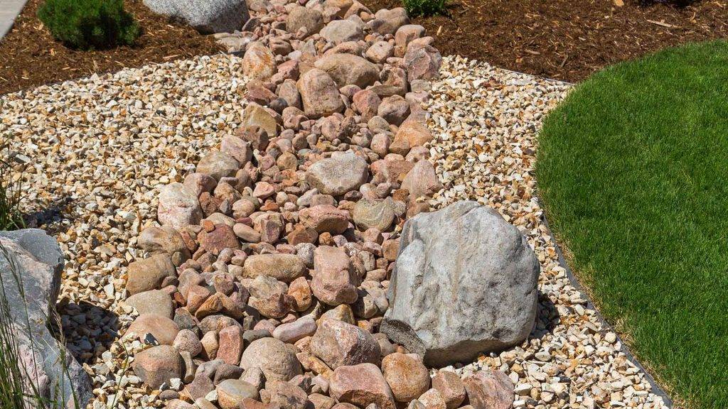 Decorative French drain system with river rocks and landscaping to prevent water pooling.