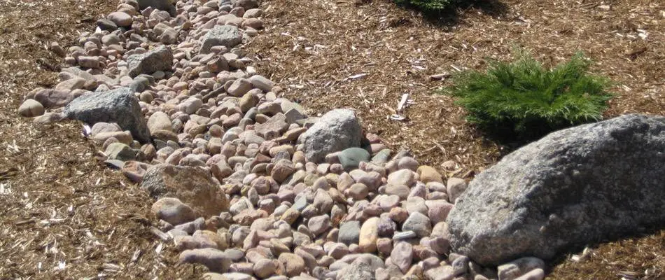 French drain system with decorative river rocks and natural landscaping for effective water drainage.