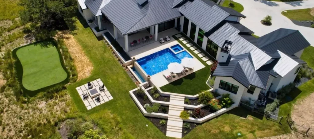 Aerial view of a luxury outdoor living space with a pool, putting green, fire pit, and custom landscaping