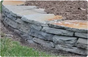 Close-up of a bluestone retaining wall with natural stone layers, enhancing a landscaped garden.